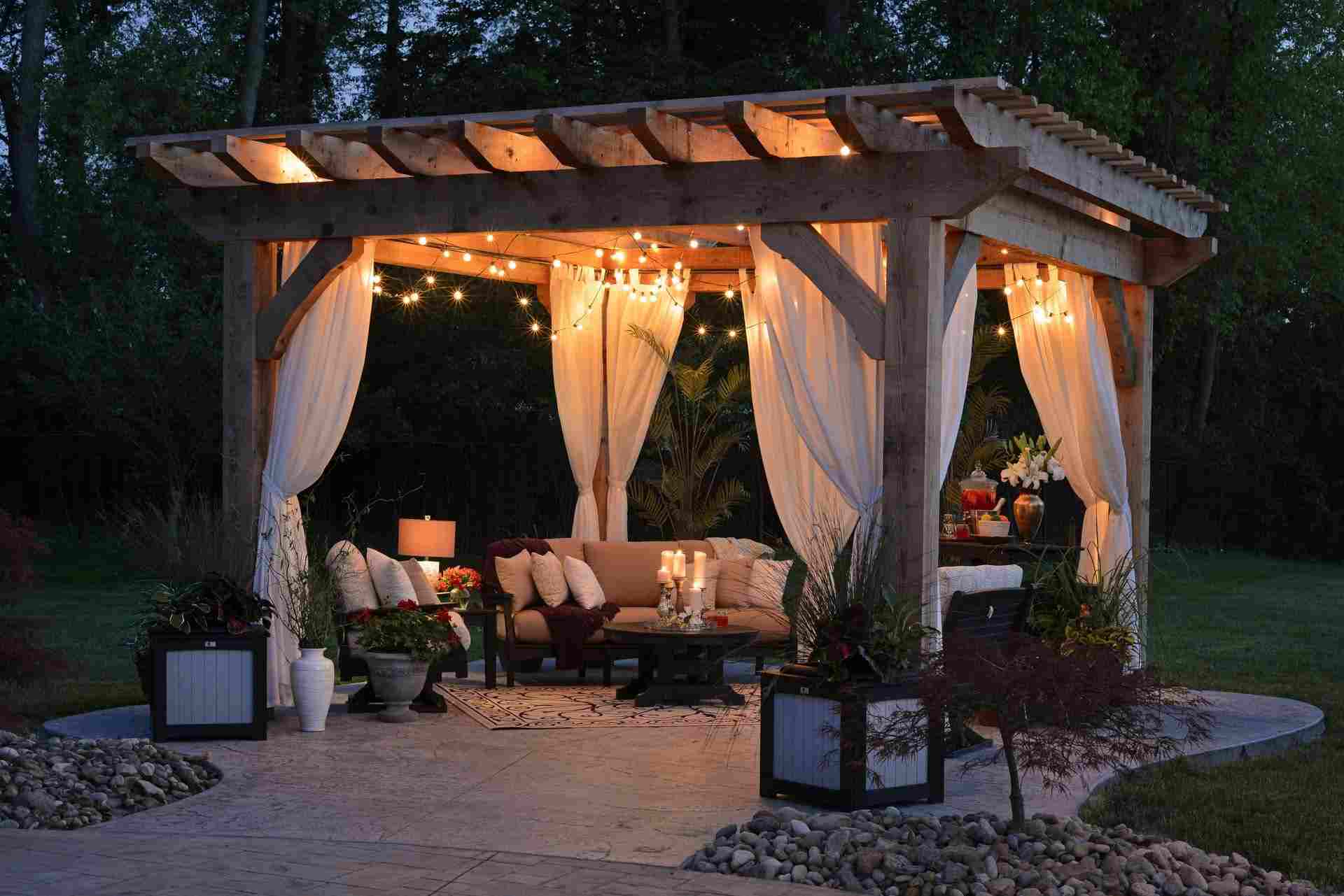A backyard pergola complete with lights, curtains, seating, and plants. 