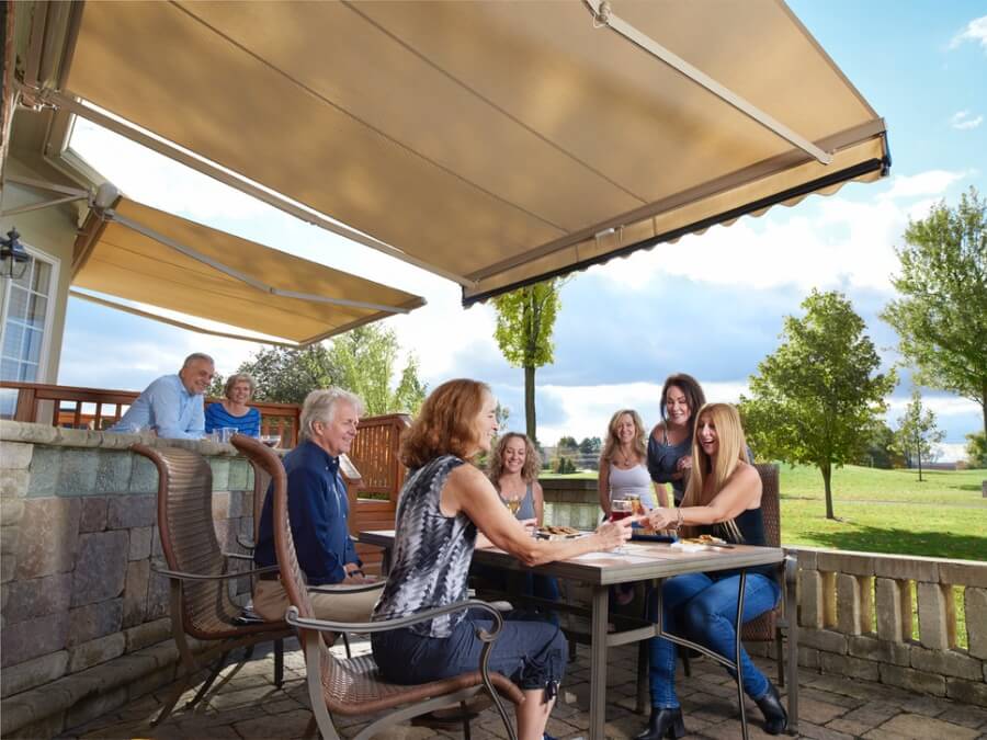 Family enjoys a gathering outside covered by a beige retractable awning.