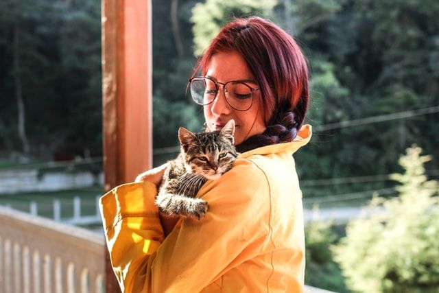 Woman with a yellow jacket holding a cat. The cat is resting its head on her shoulder