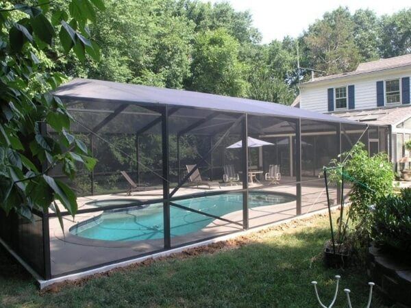 Screened pool enclosure covers the pool and patio of a backyard, offering shade and keeping out bugs and lawn litter.