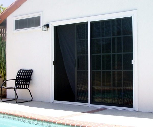 Baack door of a white painted home with double screen doors and a black patio chair.