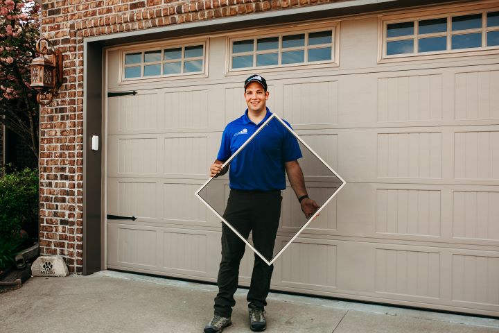 A Screenmobile service technician in holds a window screen in front of a garage door.